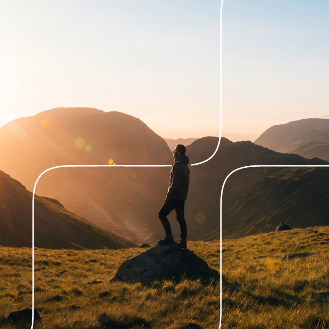 Hiker standing on a rock, looking out over mountains at sunset