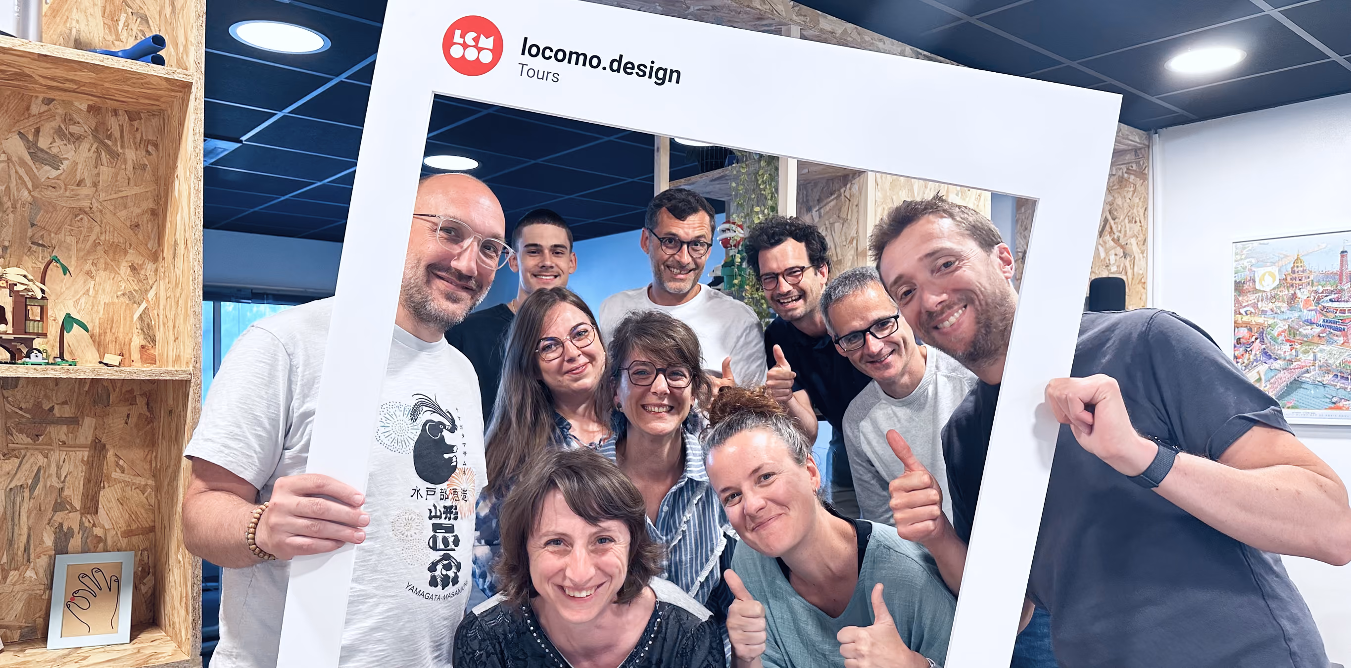 Groupe souriant, pouces levés, derrière un cadre Instagram « locomo.design » dans les locaux de l'agence