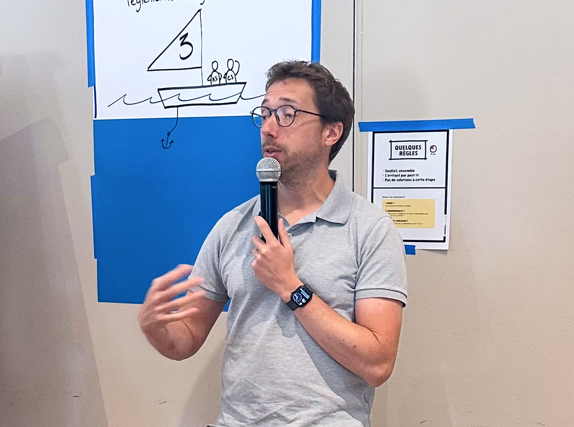 Homme parlant au micro devant un paperboard et un mur bleu