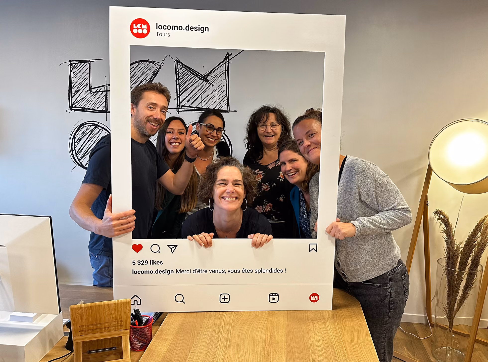 Groupe souriant derrière un cadre Instagram « locomo.design »