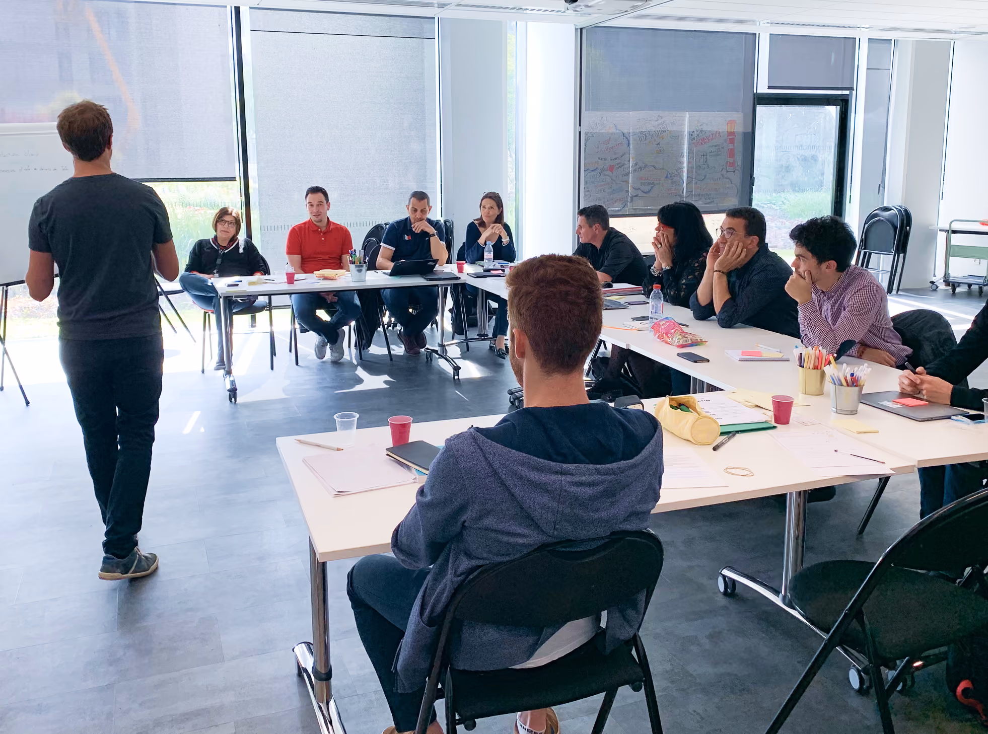 Salle de formation : un animateur debout face à des participants assis autour de tables