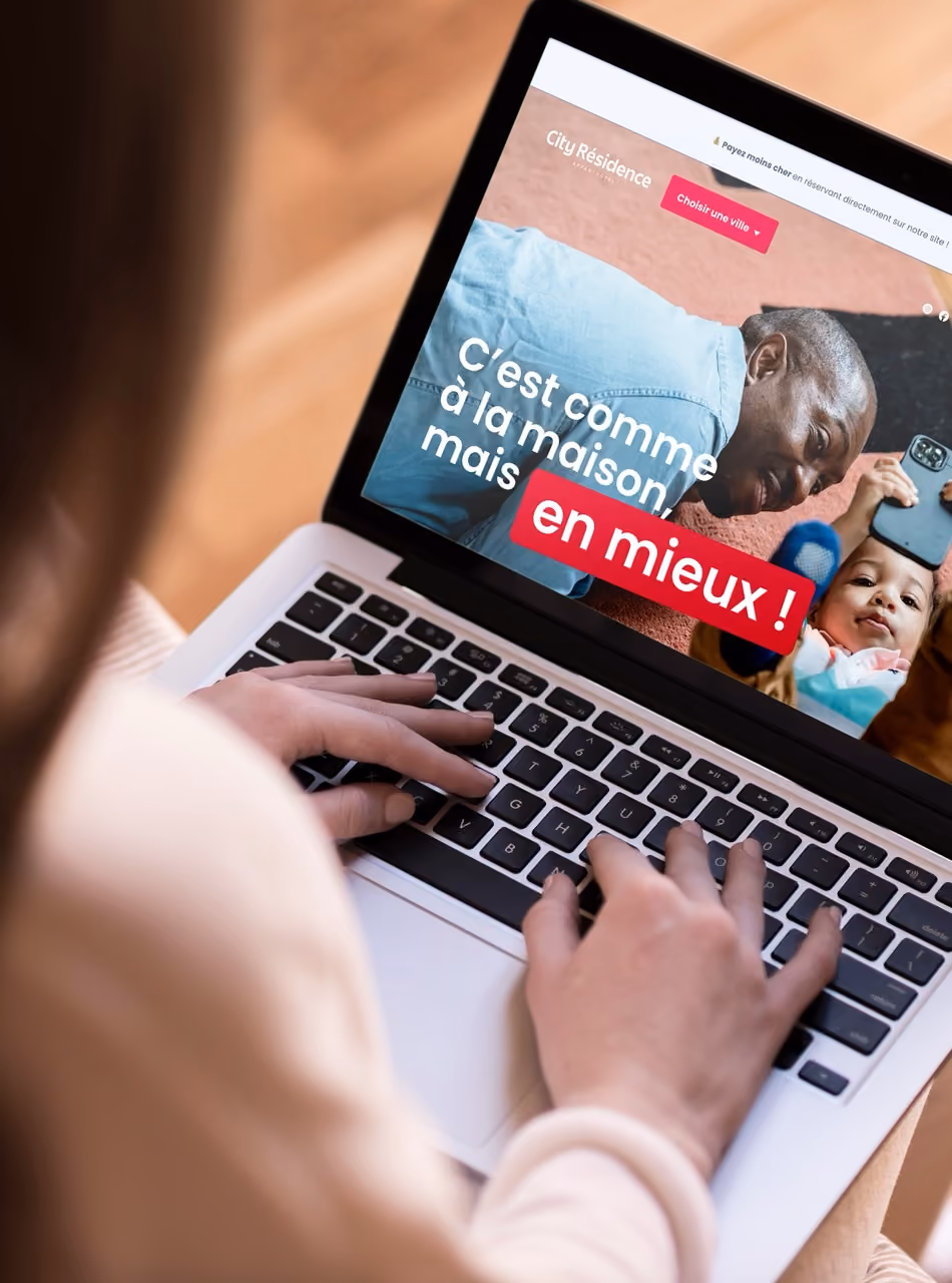 Une personne tape sur un ordinateur portable affichant un site : « C'est comme à la maison, mais en mieux ! »