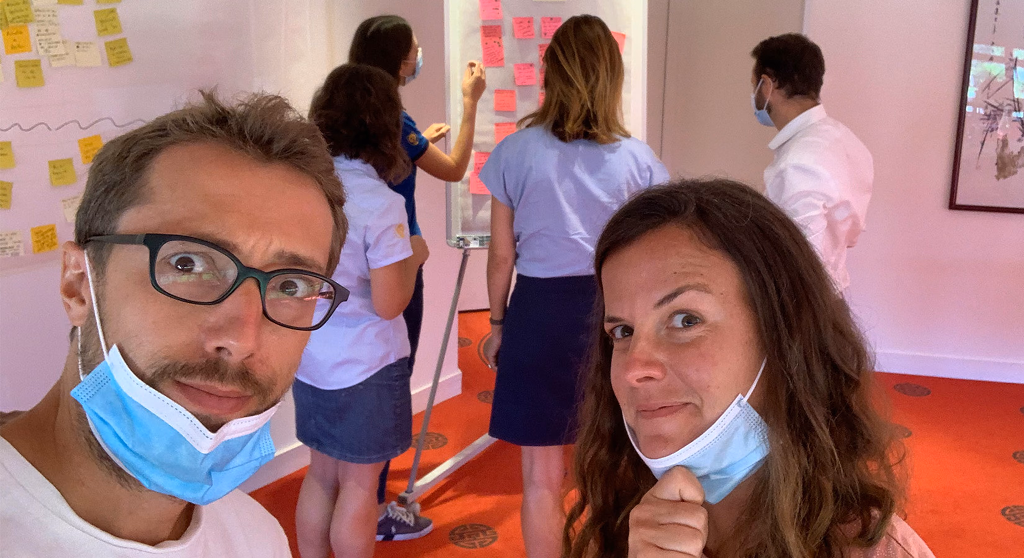 Deux personnes masquées au premier plan, d'autres collant des post-it en arrière-plan