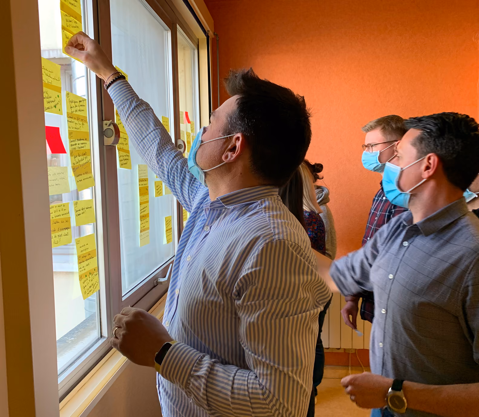 Participants masqués collant des post-it sur une fenêtre lors d'un atelier
