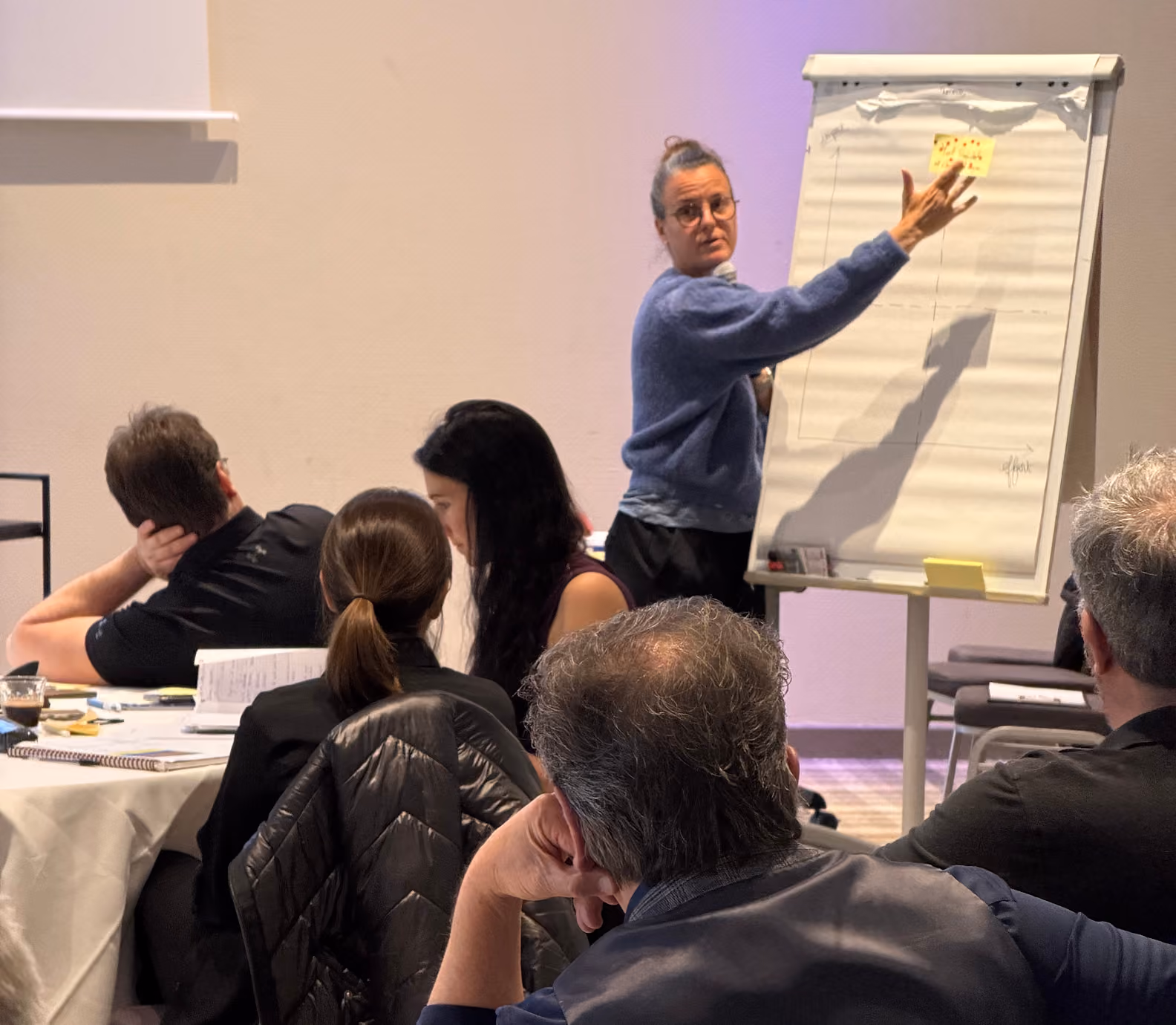 Une animatrice colle un post-it sur un paperboard devant des participants attentifs