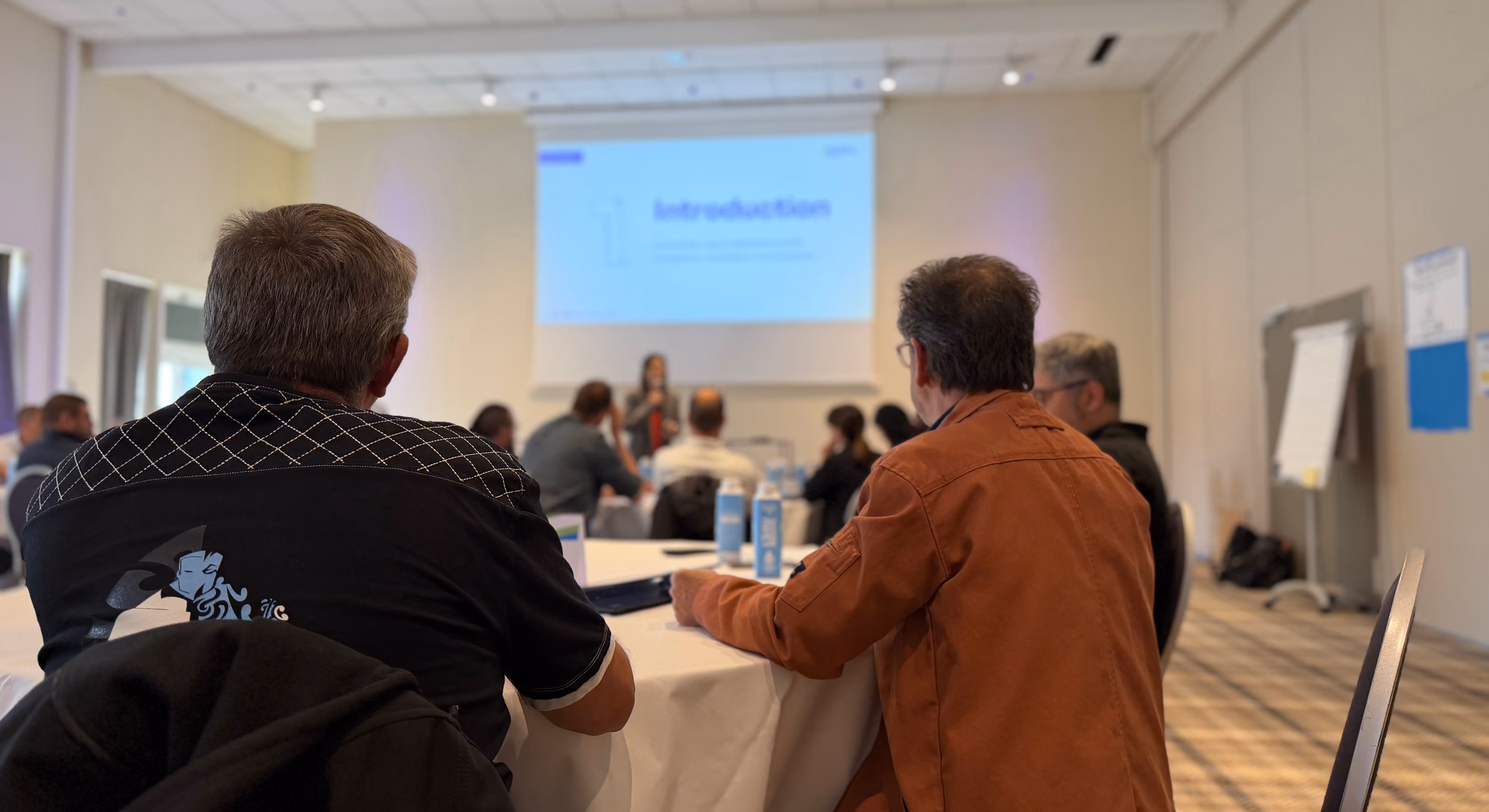 Participants vus de dos, assis en salle, devant un écran affichant « Introduction »
