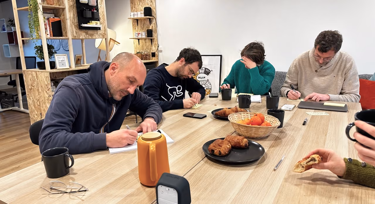 Participants assis autour d'une table en train d'écrire, avec des croissants