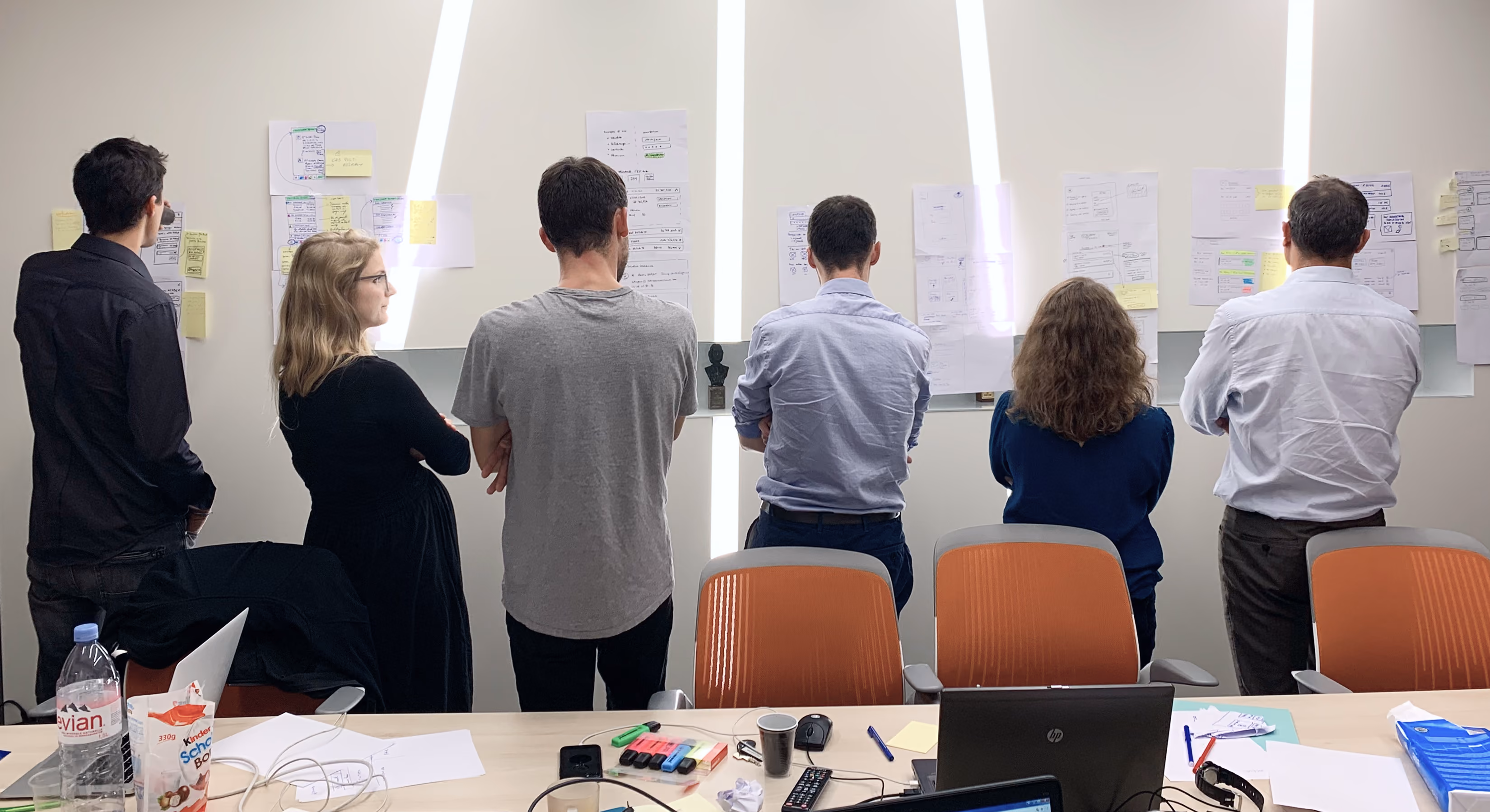 Participants debout devant des murs de post-it et de maquettes lors d'un atelier