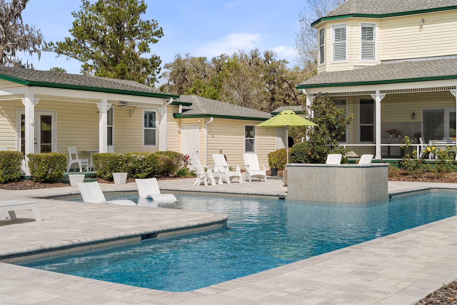Pool with a paver deck and umbrella behind a yellow historic home