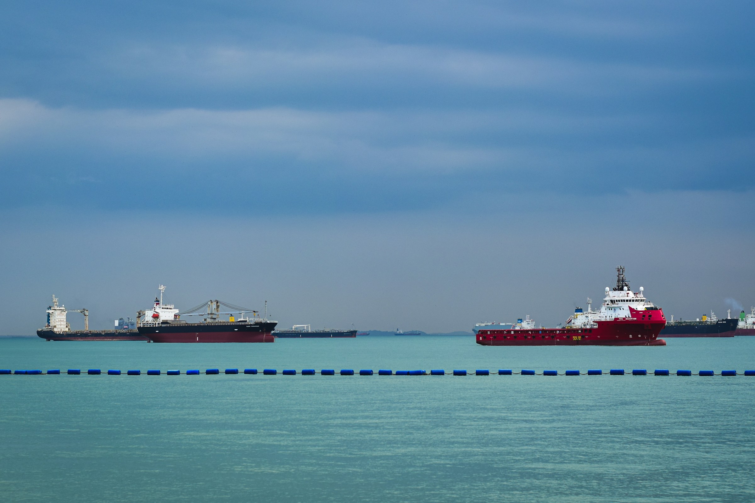 Three large cargo ships at anchor off Singapore under a broad sky