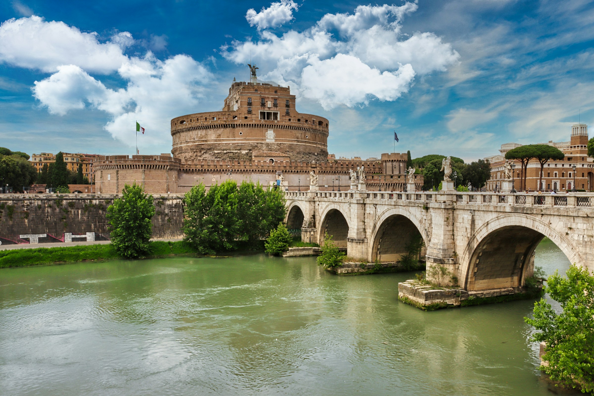 Castel Sant'Angelo seen across the Tiber river in Rome under a blue sky