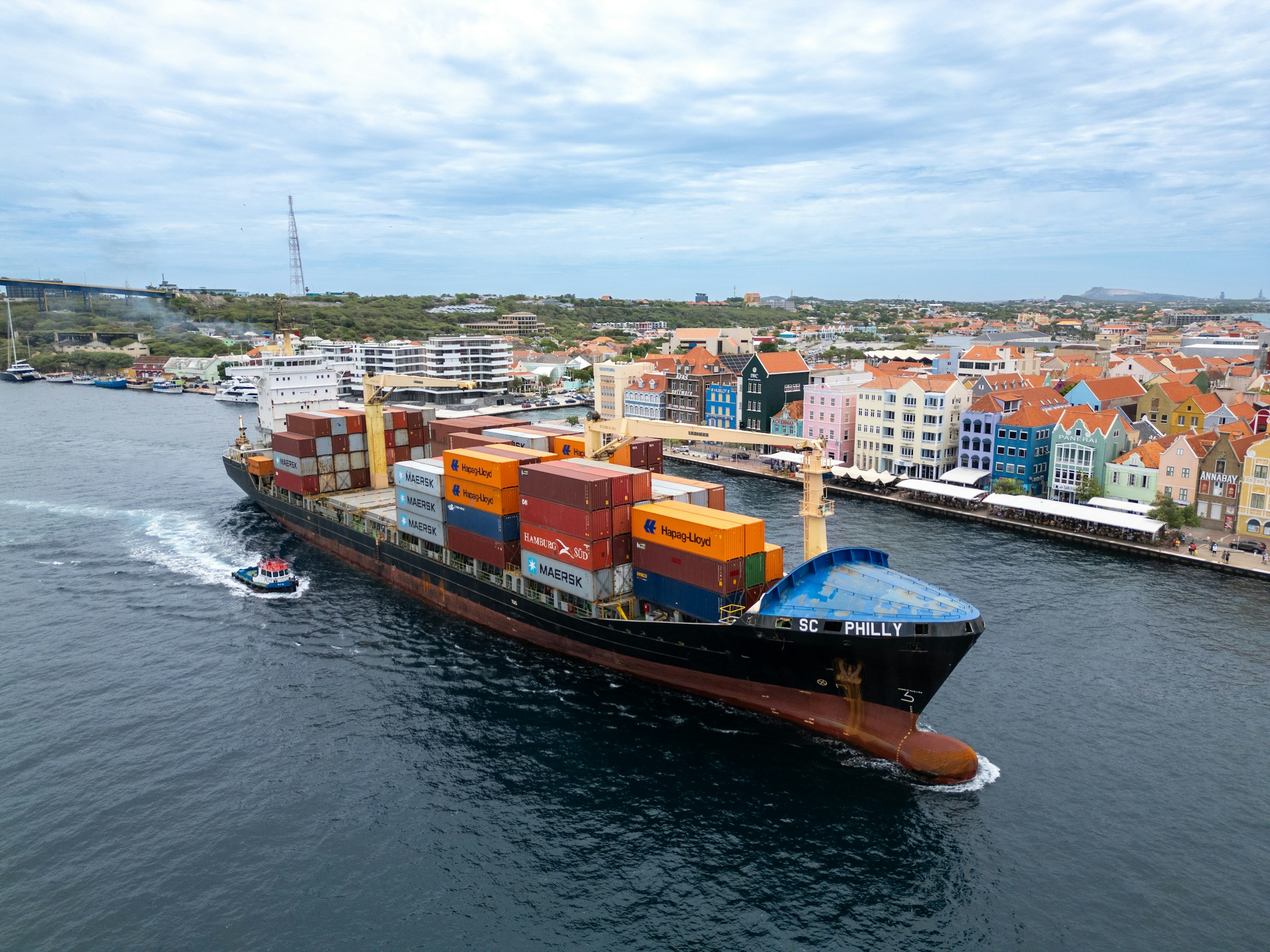 A container ship transiting the St Anna Bay channel past the coloured Handelskade waterfront in Willemstad, Curacao