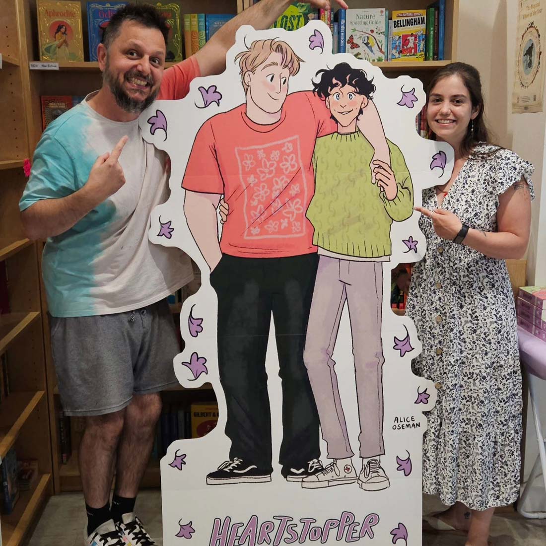 Joe and Charlie of the Story Shed photographed in front of a life size cutout illustration of two characters from Heartstopper, a graphic novel by Alice Oseman
