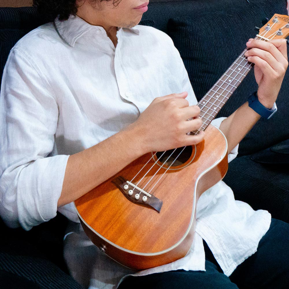 A boy us sitting and playing a ukulele