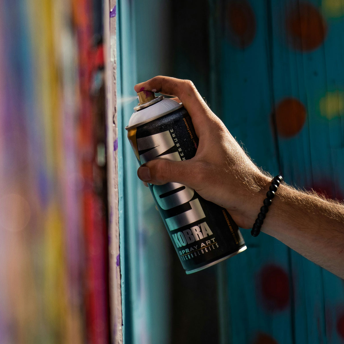 A close-up of graffiti artist’s arm applying spray paint from a can.