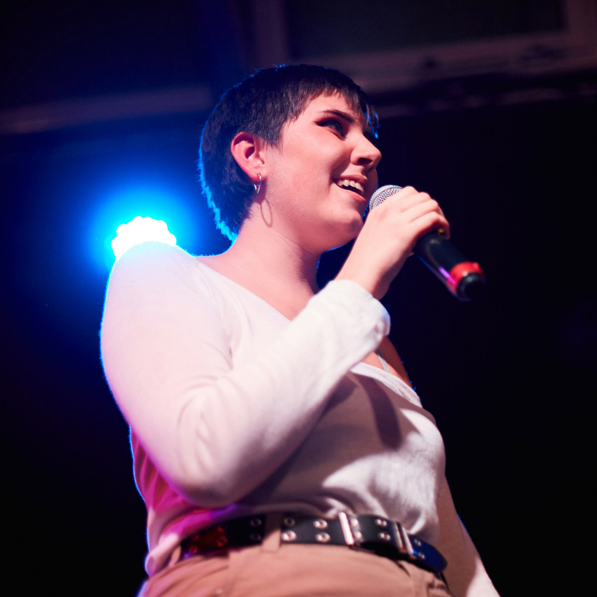 A young woman performs with a mic with stage lighting