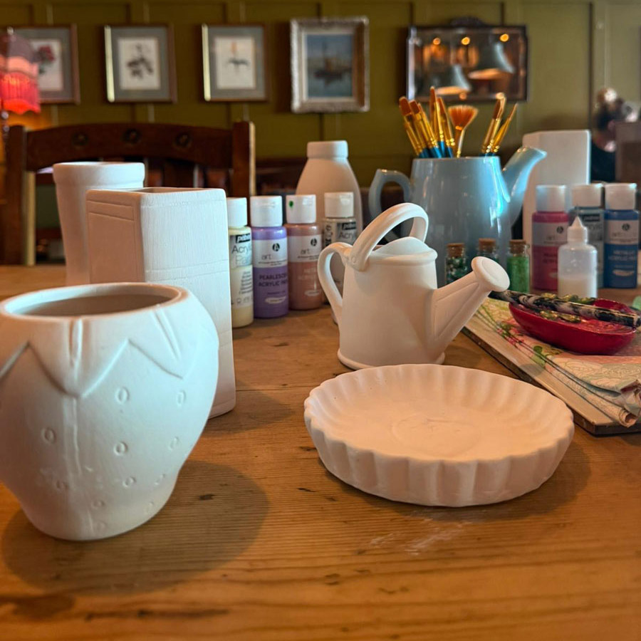 A women paints a ceramic pot at a desk.