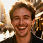 Smiling man with short curly hair and beard standing outdoors in sunlight.