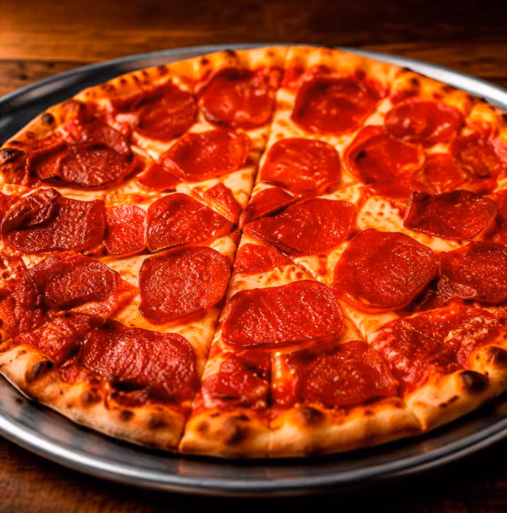 Close-up of a pepperoni pizza with melted cheese on a metal tray on a wooden table.