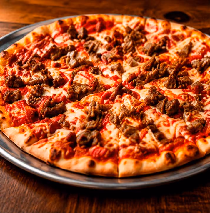 Sausage pizza sliced on a metal tray with melted cheese and tomato sauce on a wooden table.