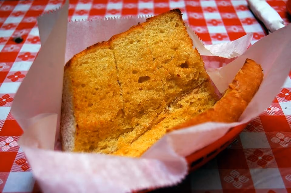 Two slices of toasted bread in a food basket lined with white paper on a red checkered tablecloth.