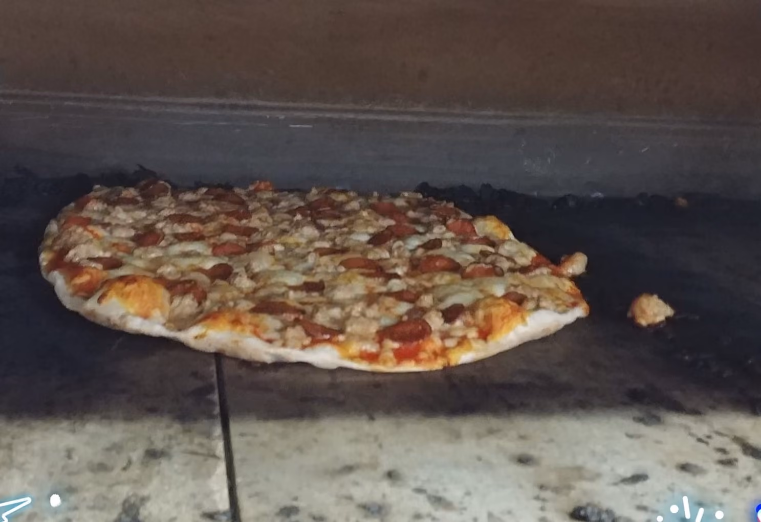 Pepperoni and sausage pizza baking on a stone surface inside an oven.