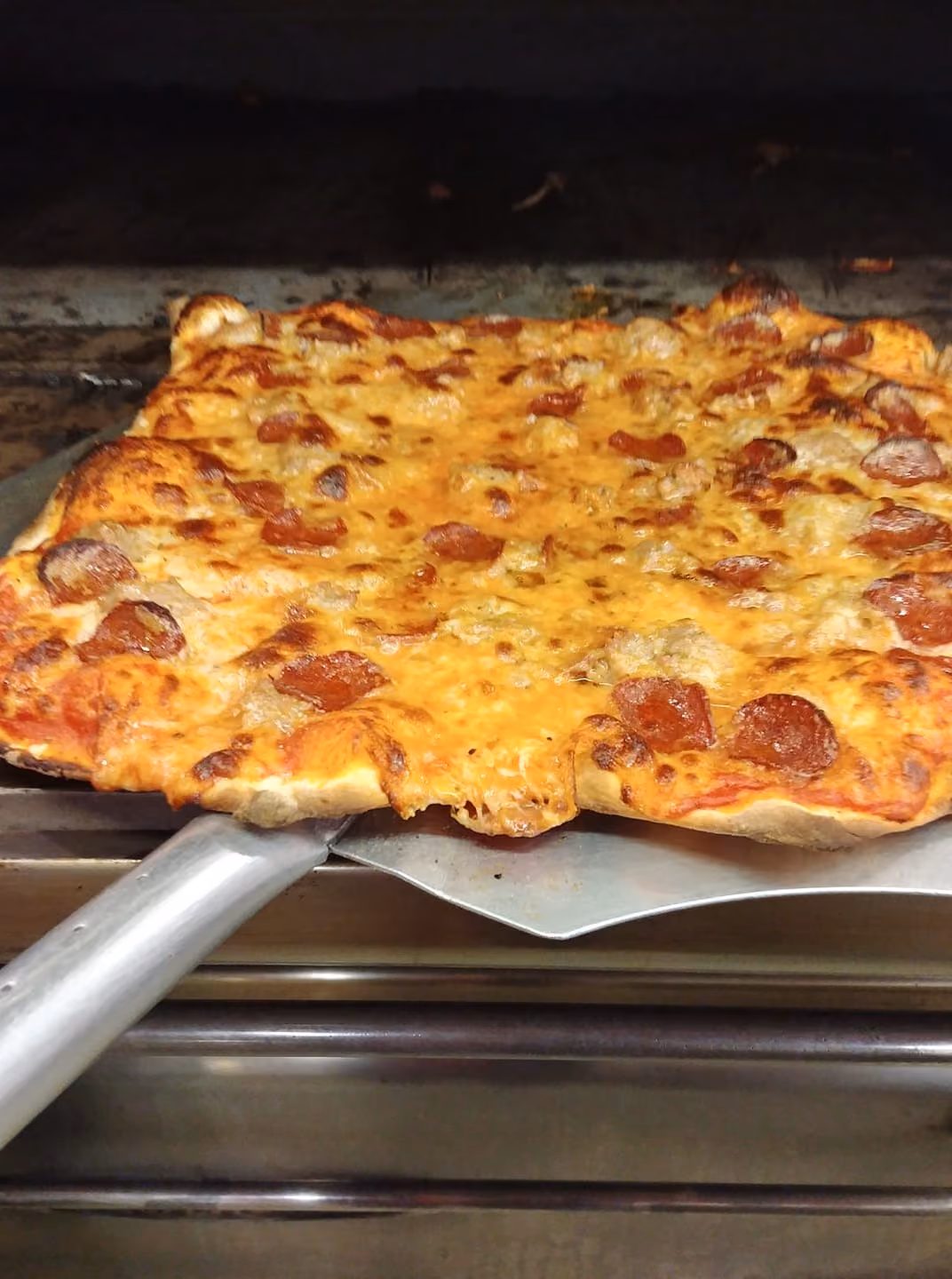 Square pepperoni pizza with melted cheese on a metal pizza peel inside an oven.