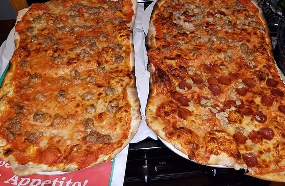 Two rectangular pizzas side by side with cheese, sausage, and pepperoni toppings on a stove.