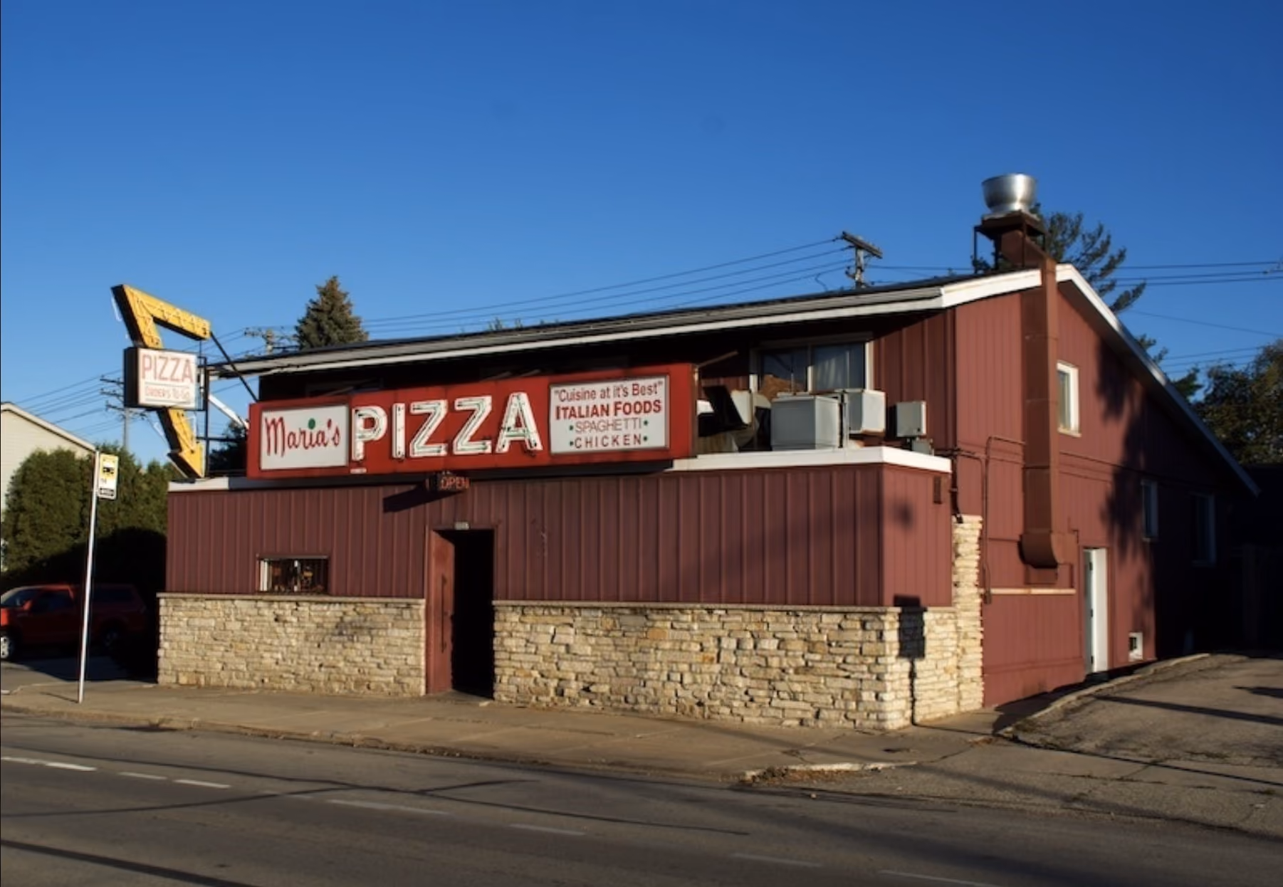 Red building with a sign reading 'Maria's Pizza' and listing Italian foods like spaghetti and chicken.