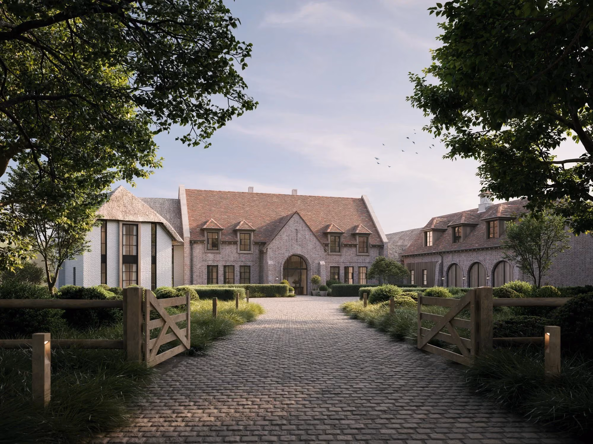 Large brick house with steep roof, arched windows, and open wooden gates along a cobblestone driveway.