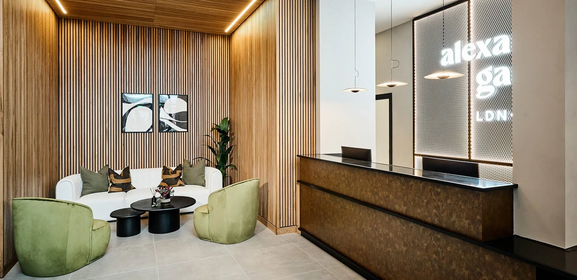 Modern reception area with wooden slat walls, white sofa, green chairs, black tables, and illuminated signage.
