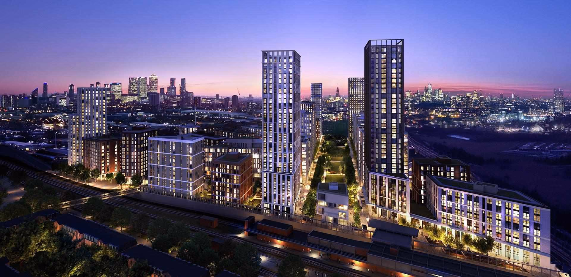 Night aerial view of modern high-rise buildings and city lights with a railway in the foreground.