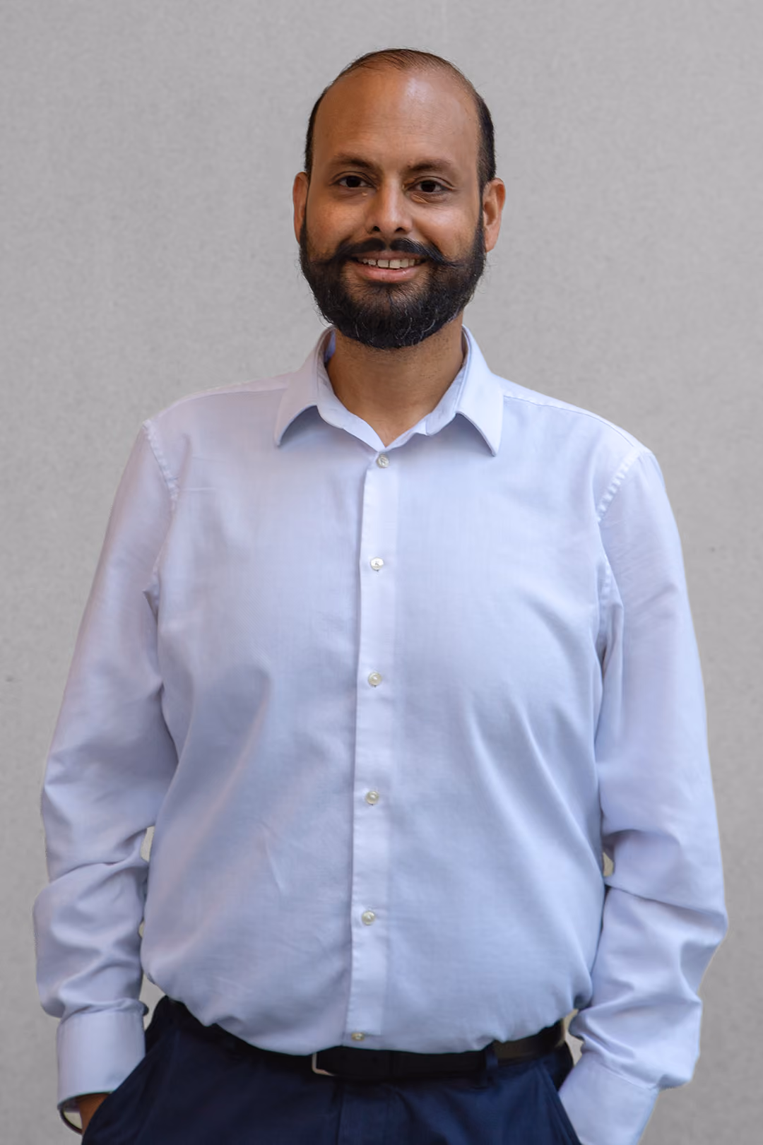 Smiling man with a beard and mustache wearing a checkered shirt over a plain t-shirt.