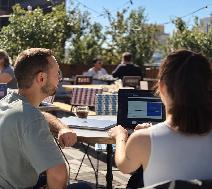 Deux membres de l'équipe Ouiflow travaillant sur ordinateur en terrasse