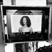 Woman with curly hair posing in front of a camera monitor.