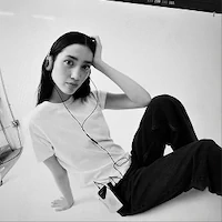 Person sitting with headphones, wearing a white shirt and black pants.