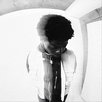 Young person with curly hair looking down in a stylized black-and-white setting.