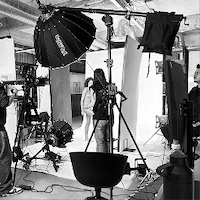 A black and white behind-the-scenes photo of e-commerce photography at LRP studios, showing a model posing on set surrounded by crew members, cameras, and large lighting equipment.