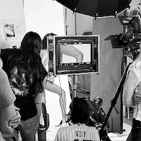 A black and white behind-the-scenes photo of e-commerce photography photoshoot at LRP studios, showing crew members reviewing a shot of a posing model on a production monitor.