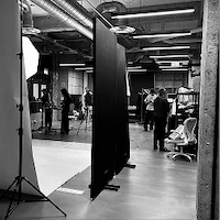 A black and white wide shot of an e-commerce photography set at LRP studios, showing crew members working around a seamless white backdrop and wardrobe staging area.