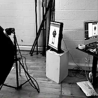 A black and white behind-the-scenes photo of a digital review station during e-commerce photography at LRP studios, showing a vertically oriented monitor on a white box displaying an image of a model.
