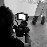 A black and white behind-the-scenes photo of e-commerce photography at LRP studios, showing an over-the-shoulder view of a photographer holding a camera and framing a shot of a model.