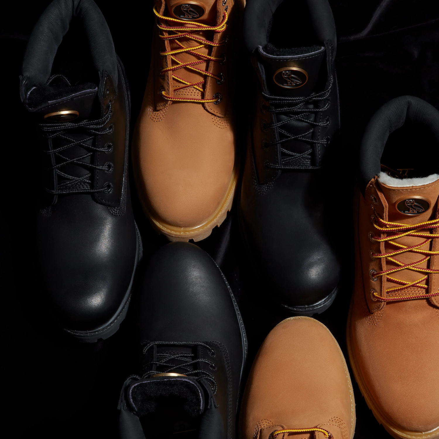 Top-down view of the OVO x Timberland boot collection in black leather and wheat suede colorways, showcasing the premium materials, signature patterned and tonal laces, and the gold OVO owl logo tongue badges.
