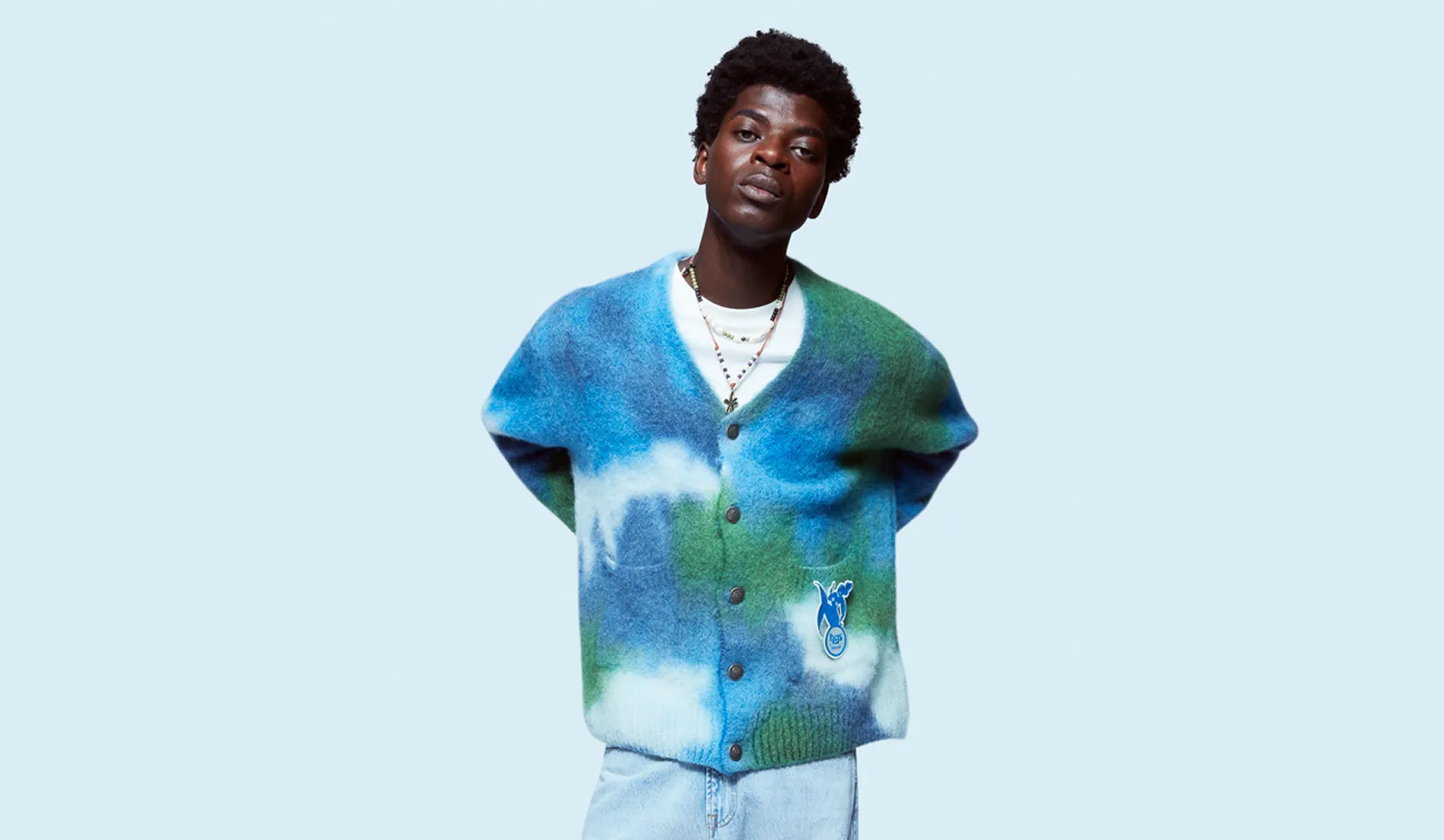 LRP model wearing a blue and green fuzzy cardigan with cloud patterns and light jeans against a light blue background.