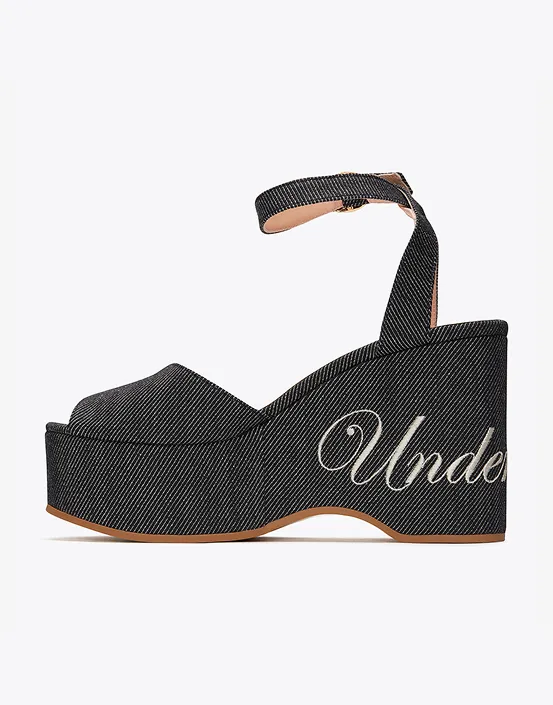 Black denim wedge sandal with ankle strap and white script embroidery on the platform heel.