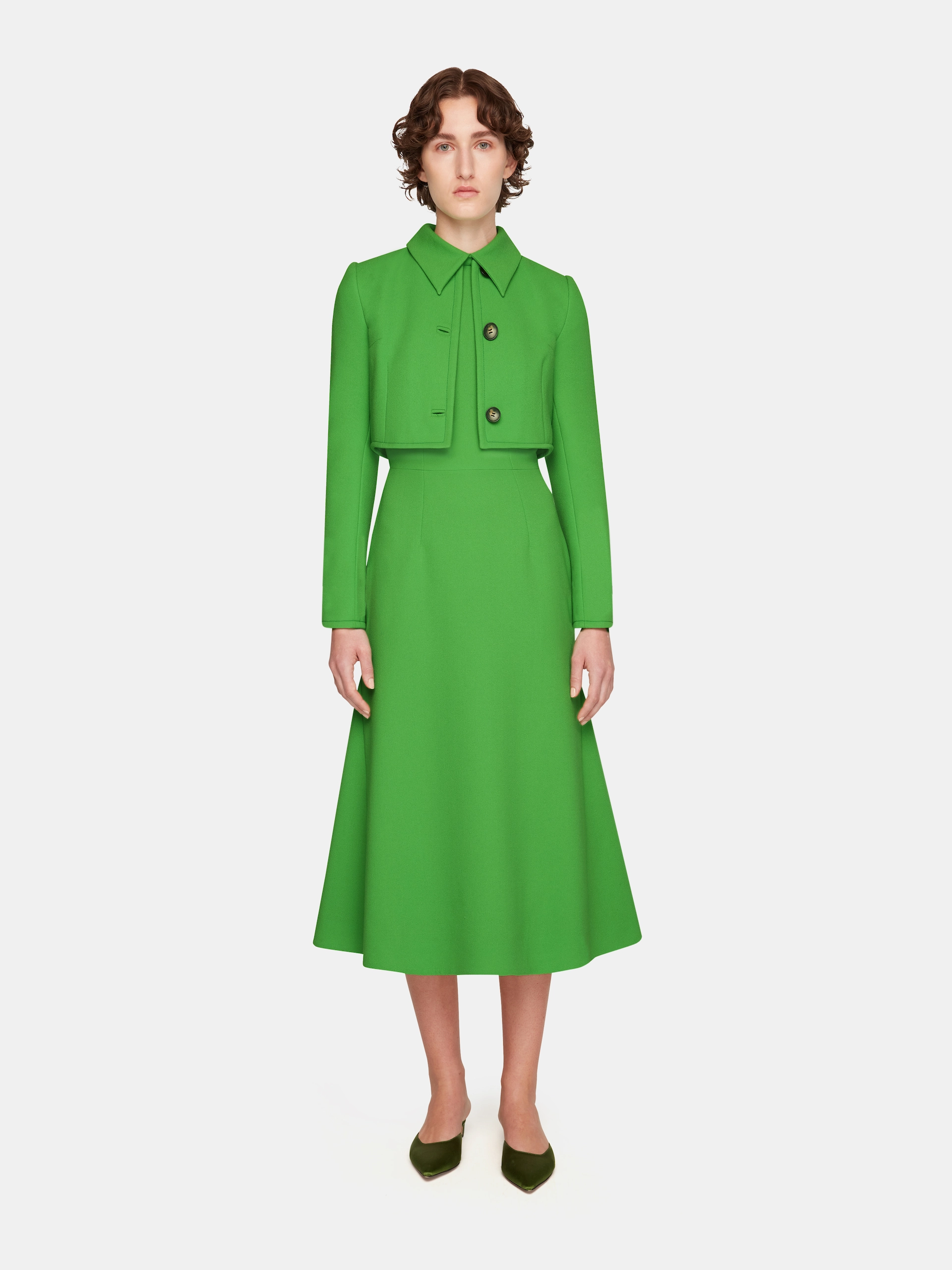 Woman wearing a bright green Emilia Wickstead dress with a cropped matching jacket and green pointed shoes.
