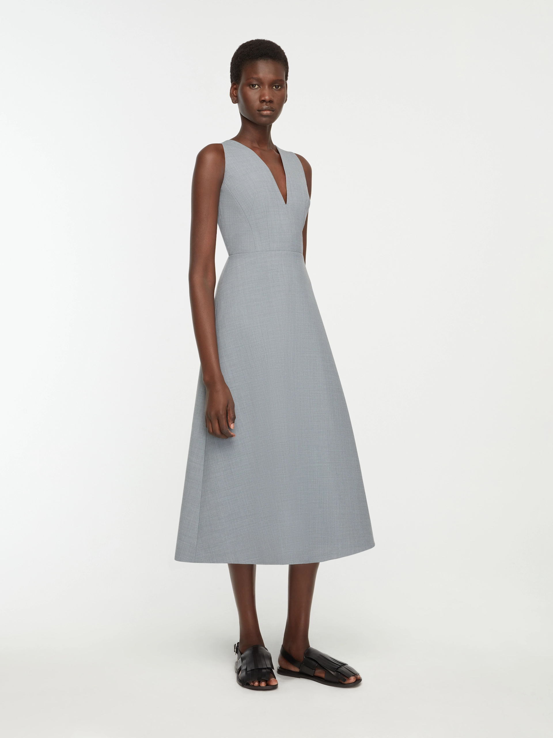 Model wearing a sleeveless, light gray, V-neck midi Emilia Wickstead dress with black flat sandals.