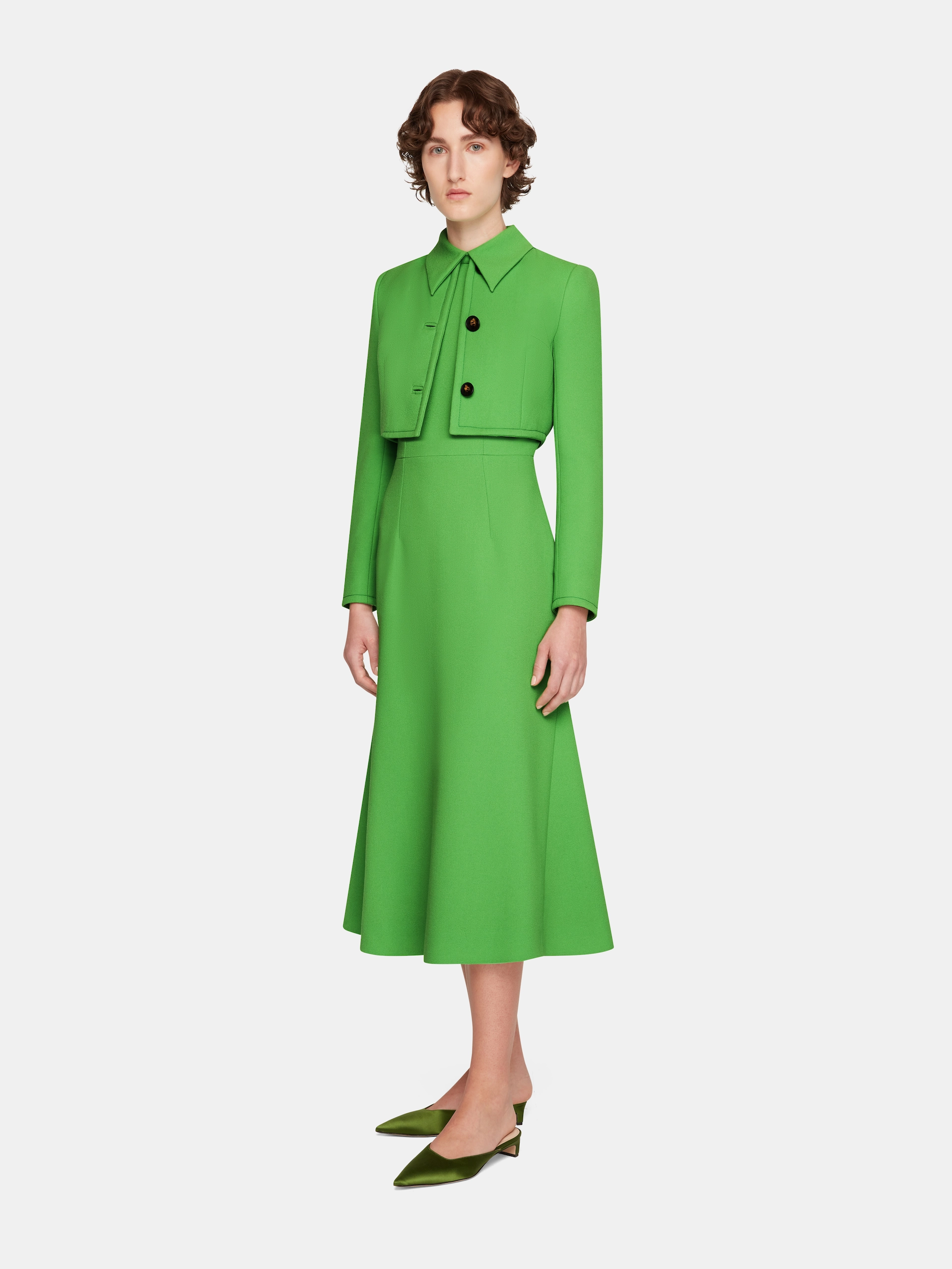 Person wearing a bright green Emilia Wickstead midi dress with a matching cropped jacket and green pointed shoes.