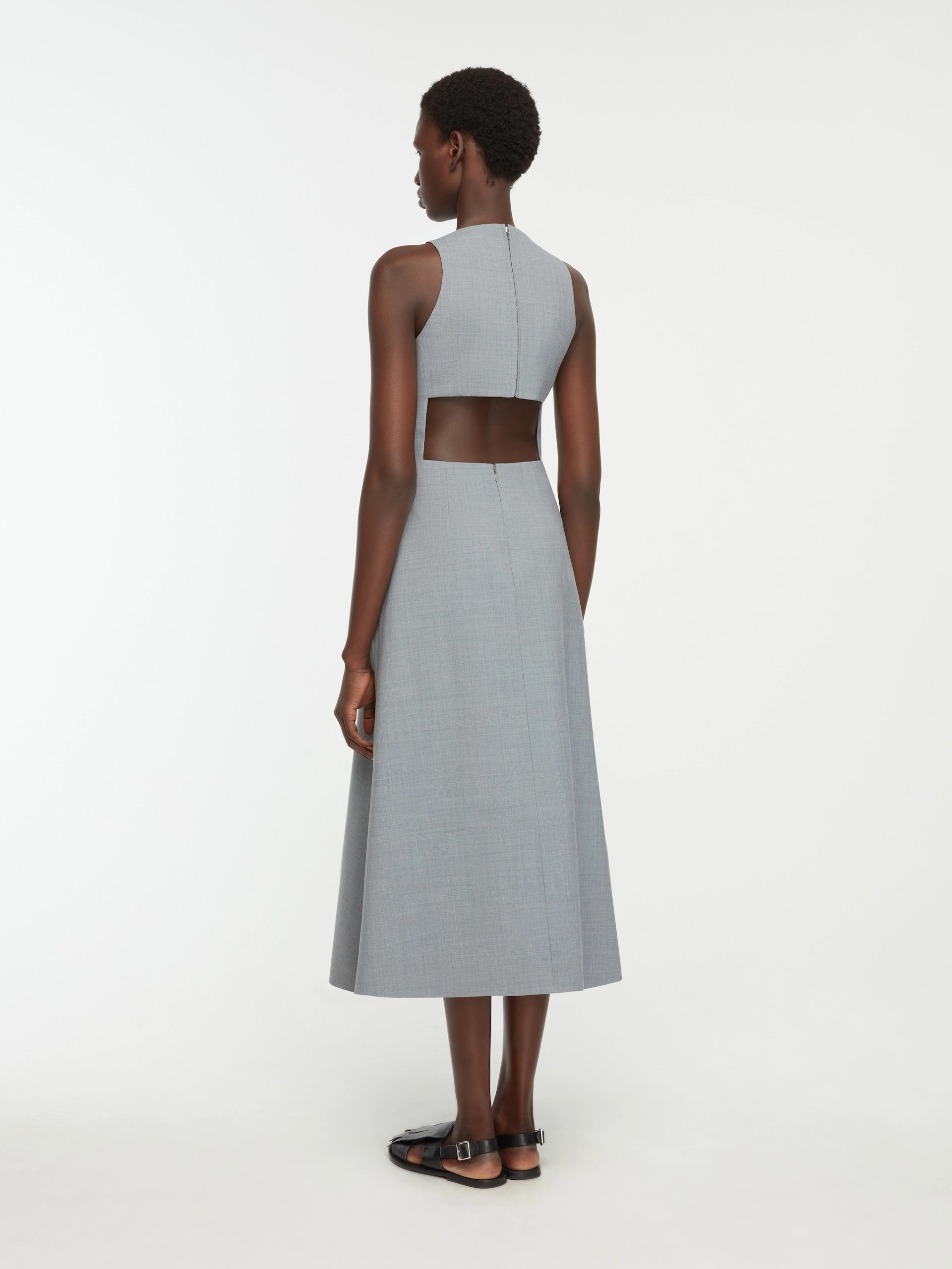 Back view of woman in sleeveless gray Emilia Wickstead dress with mid-back cutout and black sandals.