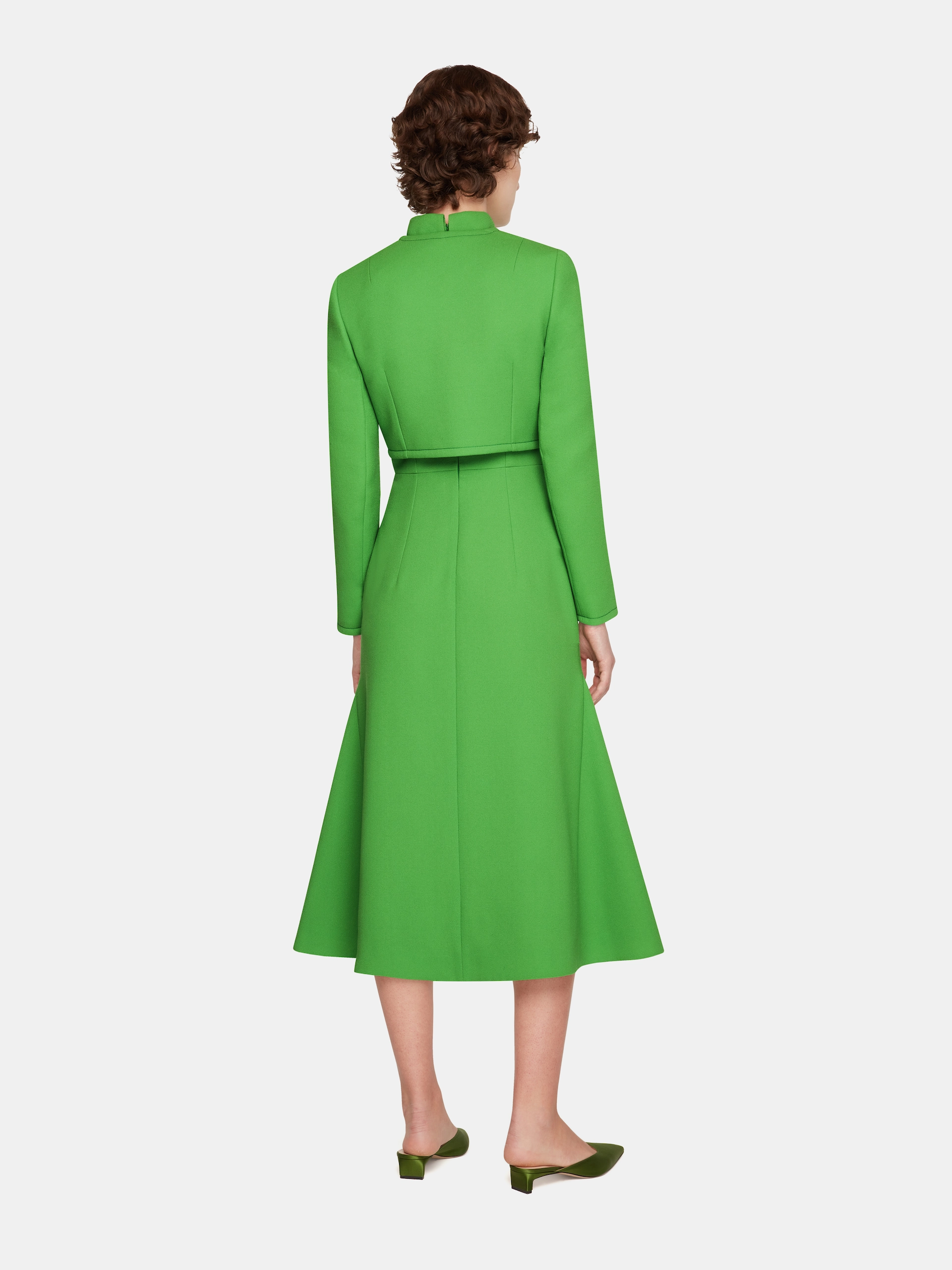 Woman seen from behind wearing a bright green Emilia Wickstead midi dress with long sleeves and green heels.